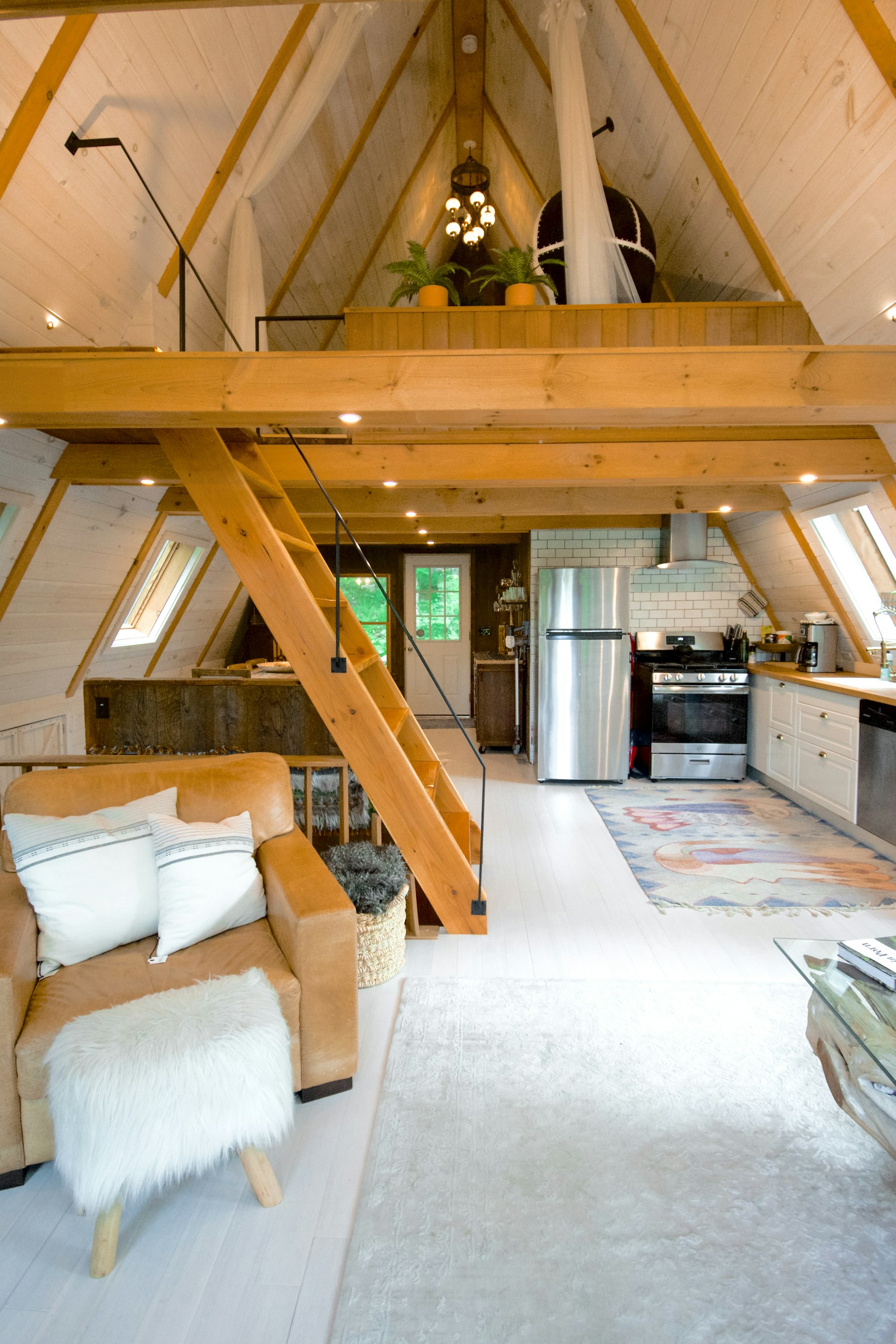 Interior of an A-frame cabin with exposed Douglas fir rafters, a loft, and a compact kitchen under the slope