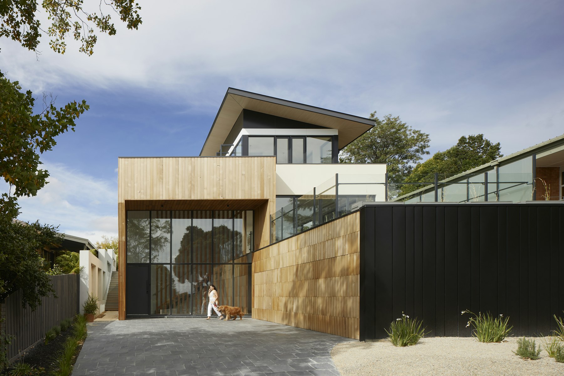 Two-storey house clad in vertical cedar and blackened steel, set behind a low board-formed concrete garden wall